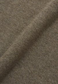 Ruskea kangas, jossa on teksturoitu neulekuvio, joka esittelee pehmeitä ja vaihtelevia sävyjä. Kangas on taitettu, mikä korostaa sen joustavaa ja sileää rakennetta.