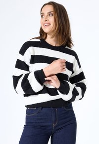 Schwarz-weißer gestreifter Strickpullover mit Rundhalsausschnitt und langen, lockeren Ärmeln. Bequeme Textur; kombiniert mit dunkelblauen Jeans.