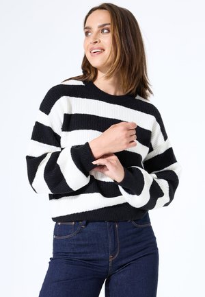Suéter de punto a rayas blancas y negras con cuello redondo y mangas largas y holgadas. Textura acogedora; combinado con jeans de color azul oscuro.