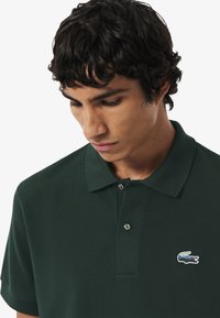 Groene poloshirt van een gestructureerde stof, met een placket met twee knopen en een geborduurd krokodillenlogo op de linkerborst.