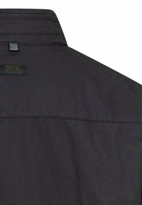 Czarna kurtka od tyłu, pokazująca kołnierz, szew górnego karczka oraz małą czarną pętlę materiałową z etykietą marki camo.