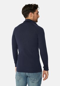 Marineblaues Langarmoberteil mit hohem Kragen, aus weichem Stoff gefertigt. Hat eine taillierte Silhouette und gerippte Bündchen, kombiniert mit hellblauen Jeans.