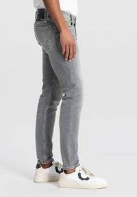 Grijze slim-fit jeans met een vervaagde wassing, voorzien van een klassiek vijf-pocket ontwerp. Gepaard met witte sneakers met marineblauwe accenten.