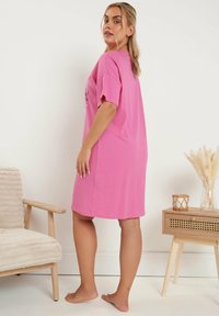 Rosa bomullsklänning med korta ärmar, avslappnad passform och rund halsringning, visad från sidan mot en neutral bakgrund.