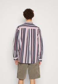 Gestreepte langarmige shirt in marineblauw, wit en rood, met een klassieke kraag en knoopmanchetten, gecombineerd met olijfgroene cargoshorts.