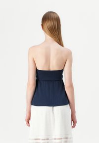 Strapless navy top with a fitted bodice, flared hem, and ribbed texture, paired with a white skirt featuring eyelet detailing and lace trim.