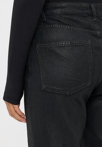 Jeans de mezclilla negra con una textura suave, que cuentan con un bolsillo trasero y un corte recto, mostrando detalles de costura mínimos.