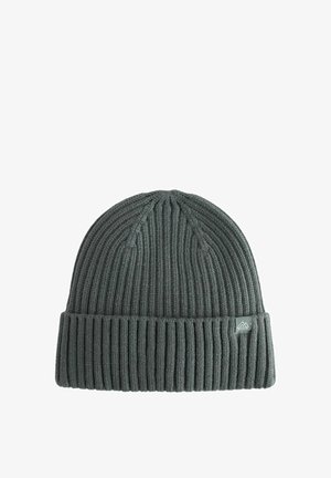 Bonnet en tricot gris avec une texture côtelée et un revers roulé, arborant un petit patch logo sur le côté. Tissu doux offrant un ajustement confortable.