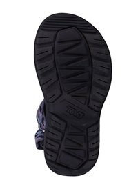 Semelle de chaussure en caoutchouc noir avec un motif de traction texturé ; elle présente des rides, des rainures et un logo embossé sur le côté.