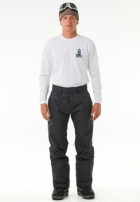 Zwarte sneeuwbroeken in combinatie met een wit longsleeve shirt met een logo. Draagt een beanie en skig goggles. Gelaagd stof met een losse pasvorm.
