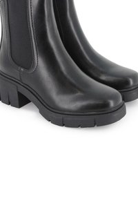 Botas negras de tobillo hechas de cuero suave, con paneles laterales elásticos, punta redondeada y una suela de goma gruesa con surcos.