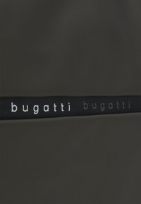 Tecido preto com uma textura suave, apresentando uma faixa horizontal onde está o nome da marca "bugatti" em letras prateadas.