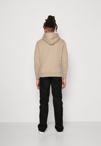 Beige hettegenser med kengurulomme og snorhette, parret med svarte bukser og hvite joggesko. Glatt tekstur, avslappet passform.