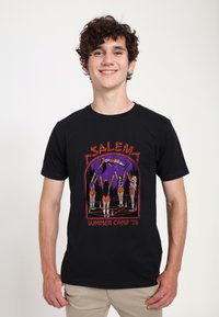 Černé bavlněné tričko s barevným grafickým designem postav na táboře, na fialovém pozadí, označené "Salem Summer Camp '78."