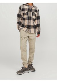 Ruudullinen flanellipaita sävyissä tan, laivastonsininen ja harmaa, jossa kaksi rintataskua; yhdistetty beigenvärisiin kapeneviin housuihin ja harmaisiin urheilukenkiin.