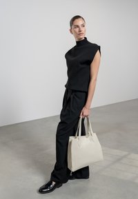 Top negro de manga corta combinado con pantalones oscuros de cintura alta y zapatos negros brillantes, sosteniendo un bolso de cuero crema.