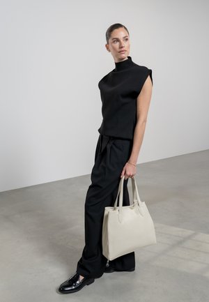 Un haut noir à manches courtes associé à un pantalon sombre taille haute et des chaussures noires brillantes, tenant un sac fourre-tout en cuir crème.