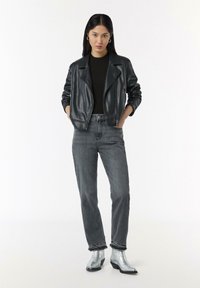 Schwarze Lederbikerjacke, gerippter schwarzer Pullover, graue Jeans und metallisch silberne Knöchelstiefel. Gerade Passform mit Reißverschluss- und Bunddetails.
