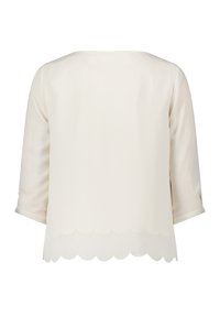 Blouse à manches longues de couleur crème avec un ourlet festonné et des poignets roulés, vue de dos sur fond blanc.