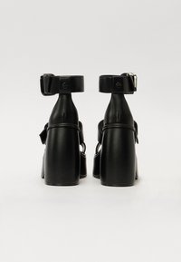 Svarta högklackade skor med en kraftig design, tillverkade av läder, med en ankelrem och spänne samt en slät yta.