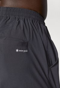 Black shorts made of lightweight fabric, featuring an elastic waistband, side pockets, and a back pocket with the "snow peak" logo.