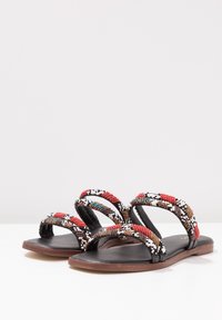 Svart sandalet med pärlor som har en platt sula, dubbla remmar prydda med ett färgglatt mönster av röda, vita och blå pärlor samt en slät yta.