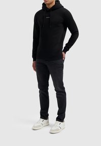 Zwarte hoodie van katoenmix met zak aan de voorkant en koorden, gecombineerd met donkere Jeans en witte sneakers.