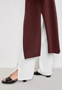 Top bordeaux con spacchi laterali abbinato a pantaloni bianchi larghi. Sandali aperti neri con tacco basso. Tessuti semplici e texture.