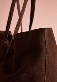 Brown suede tote bag with smooth texture, simple design, and two shoulder straps. Features visible stitching along edges.