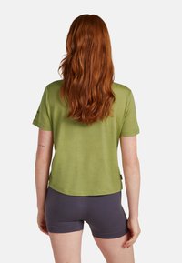 Camicia verde oliva a maniche corte con vestibilità rilassata, abbinata a pantaloni corti grigio scuro. Realizzata in tessuto leggero e strutturato.