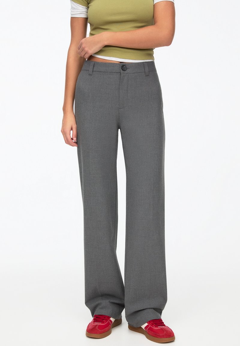 Pantalons larges gris en tissu lisse ; dotés d'une fermeture à bouton et de deux poches latérales, associés à un haut vert et des baskets rouges.