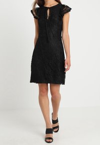 Svart spetsklänning med korta volangärmar, nyckelhålsringning, figursydd överdel och utsvängd kjol. Bärs med svarta klacksandaler.