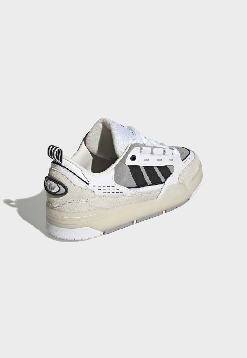 Białe sneakersy z szarymi zamszowymi akcentami, czarnymi paskami i amortyzowaną podeszwą. Posiadają sznurowaną konstrukcję oraz teksturowany tył.
