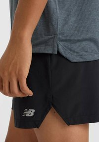 Lichtgewicht grijs sportshirt met een gestructureerd patroon, gecombineerd met zwarte shorts met een gesplitste zoom en reflecterend New Balance-logo.