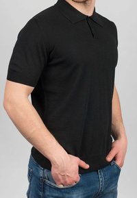 Polo nera a maniche corte con collo a risvolto, polsini a coste e tessuto a maglia liscia, indossata con jeans blu.