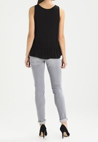 Top negro sin mangas con un dobladillo con volantes, combinado con unos jeans ajustados gris claro arremangados y tacones altos negros. Fondo neutro.
