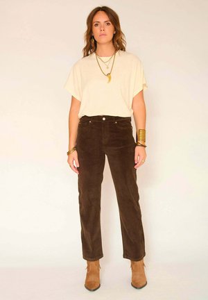 Chemise beige à manches courtes, pantalon en velours côtelé taille haute marron et bottines chelsea beige. Des bijoux en or superposés ajoutent des touches subtiles.