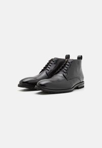 Bottines en cuir noir avec une finition lisse et texturée, bout rond et détails de laçage. Comprend un petit talon et une semelle contrastante.