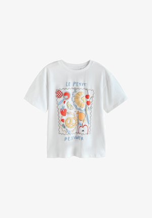 Jeune fille aux longs cheveux foncés portant un t-shirt blanc avec des illustrations colorées sur le thème du petit-déjeuner et un jean bleu ample, sur un fond jaune.