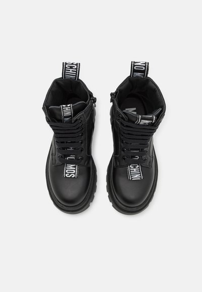 Bottes noires en cuir à chevilles avec des orteils ronds, des semelles épaisses et des lacets noirs. Présente une étiquette de logo blanche sur la languette et un détail contrastant sur les côtés.