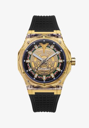 Montre-bracelet ton or avec bracelet en silicone noir texturé, cadran à motif géométrique, index des heures en gras et logo distinctif au centre.