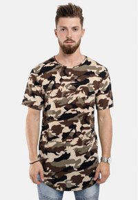 T-shirt med camouflage-mönster i beige, grön och svart; korta ärmar, rund hals och längre fåll. Mjuk bomullstyg med en avslappnad passform.