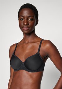 Black padded bra with adjustable thin straps, smooth surface, and a subtle lace detail along the band. Designed for comfort and fit.