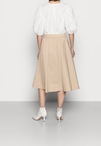 Witte blouse met pofmouwen en oogjesdetails, gecombineerd met een beige, knielange A-lijn rok en witte enkellaarsjes met een rits.