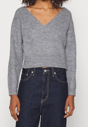 Person wearing a grey V-neck knit sweater paired with high-waisted dark blue jeans with yellow stitching details.