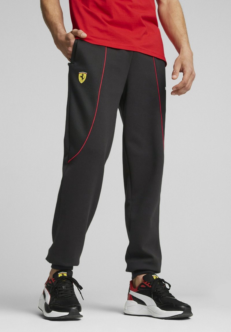 Černé sportovní kalhoty s červenými akcenty a logem Ferrari na levém boku, s tapered designem a bočními kapsami.