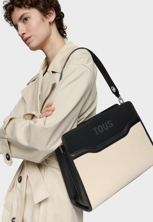 Czarna i kremowa torba typu tote z teksturowanym wykończeniem, z tłoczonym logo "TOUS" i o usztywnionym kształcie. W zestawie regulowany czarny pasek na ramię.