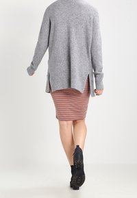 Gray knitted sweater with a high-low hem, paired with a pink striped pencil skirt. Black ankle boots complete the outfit.