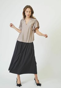 Top beige chiaro con maniche a sbuffo corte, design a V, abbinato a una lunga gonna nera plissettata e tacchi neri a punta. Stile minimalista.