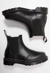 Dos botas Chelsea negras con paneles laterales elásticos y tiradores, exhibidas sobre un fondo blanco, mostrando cuero suave y suelas resistentes.